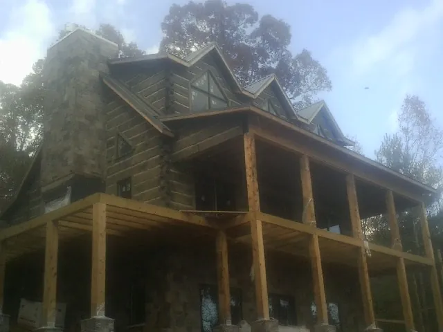 Stone chimney and dormers on a large log home with a timber porch in Bedford